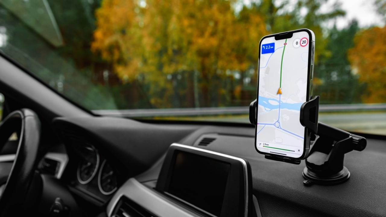 Smartphone with navigation route on screen mounted on phone holder at car dashboard.