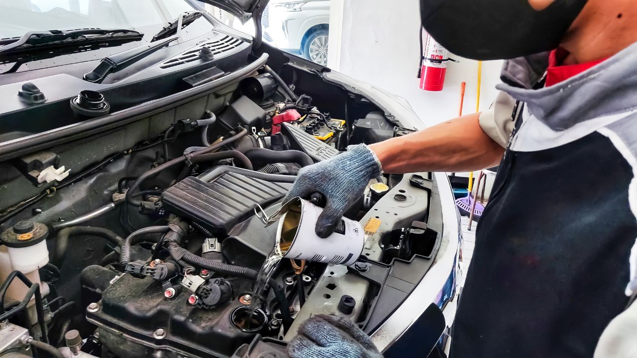 An Indonesian car mechanic is pouring engine flush liquid to a gasoline engine car in an authorized workshop dealership