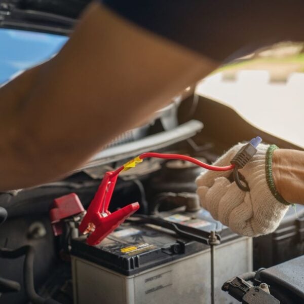 Close-up of mechanic holding voltmeter to check voltage car battery energy problem for service maintenance. Car mechanic noting repair parts during open car hood engine repair unrecognisable