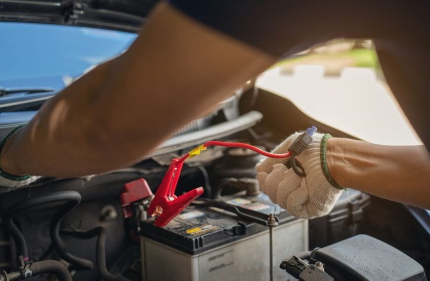 Close-up of mechanic holding voltmeter to check voltage car battery energy problem for service maintenance. Car mechanic noting repair parts during open car hood engine repair unrecognisable