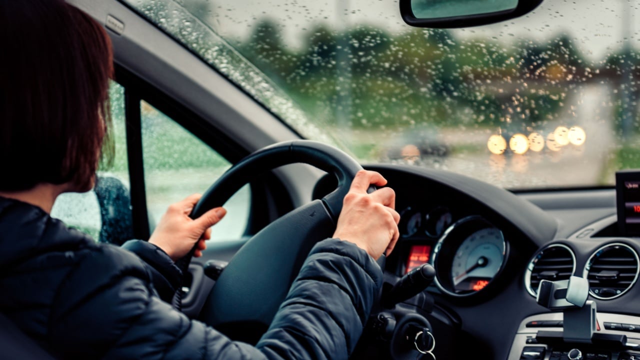 Woman wearing black jacket driving car on the motorway in the rain