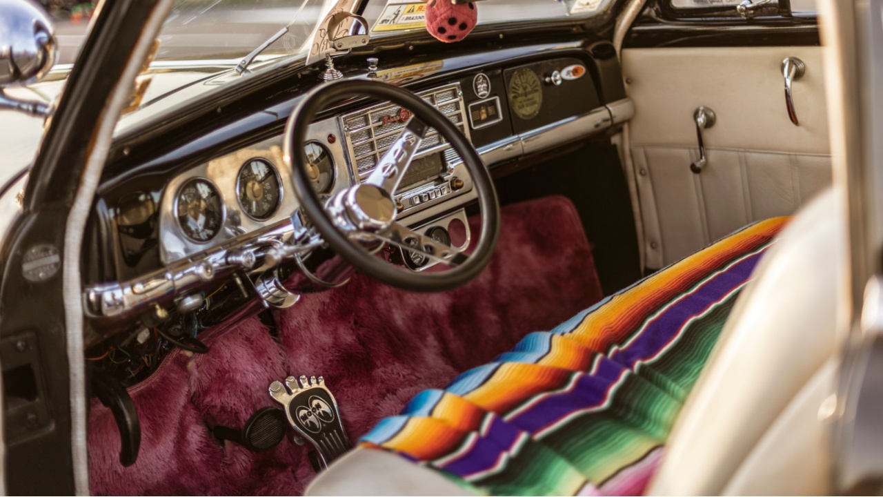 close-up of vintage plymouth car interior showcasing the steering wheel, dashboard, colorful serape seat cover, and unique details