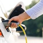 The driver of the electric car inserts the electrical connector to charge the batteries. Unrecognizable man attaching power cable to electric car. Electric vehicle Recharging battery charging port.