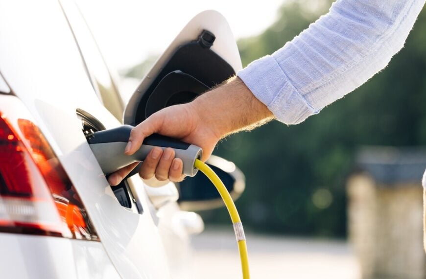 The driver of the electric car inserts the electrical connector to charge the batteries. Unrecognizable man attaching power cable to electric car. Electric vehicle Recharging battery charging port.