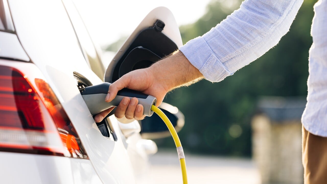 The driver of the electric car inserts the electrical connector to charge the batteries. Unrecognizable man attaching power cable to electric car. Electric vehicle Recharging battery charging port.