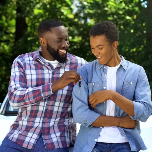 Happy dad giving car key to son, permission to drive, parenthood trust, family