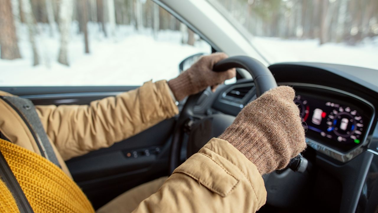 Man wearing jacket and gloves driving car in winter and snow