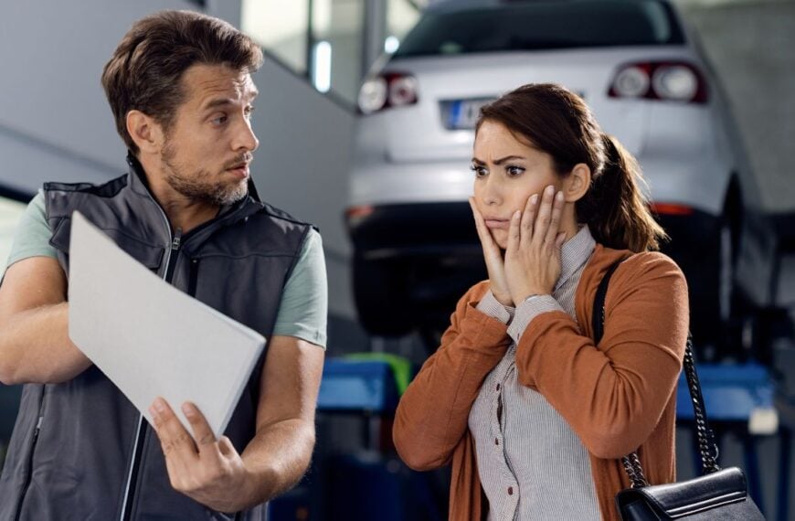 Auto mechanic showing report and car repair costs to shocked woman in a workshop.