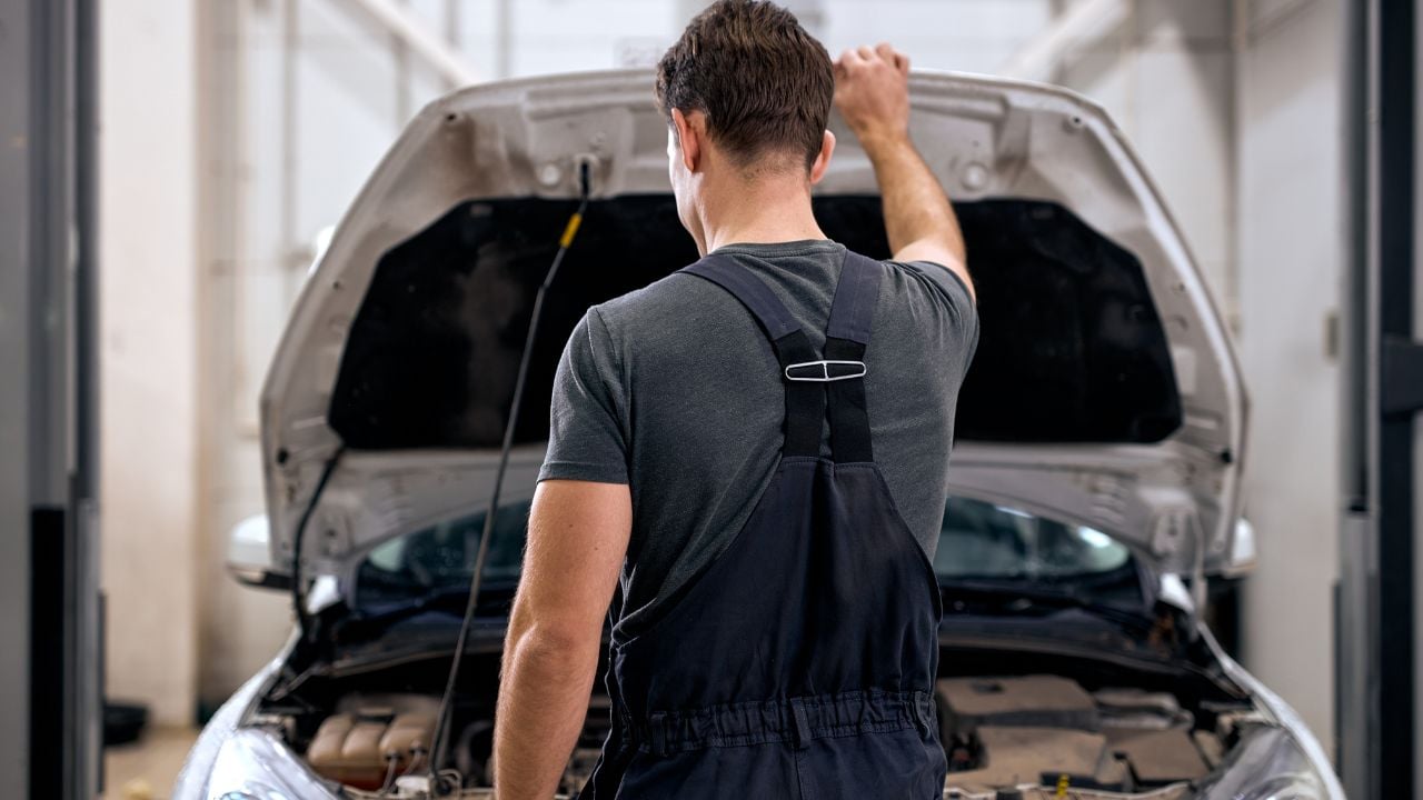 professional car mechanic working under car hood in repair garage, closing or opening the hood