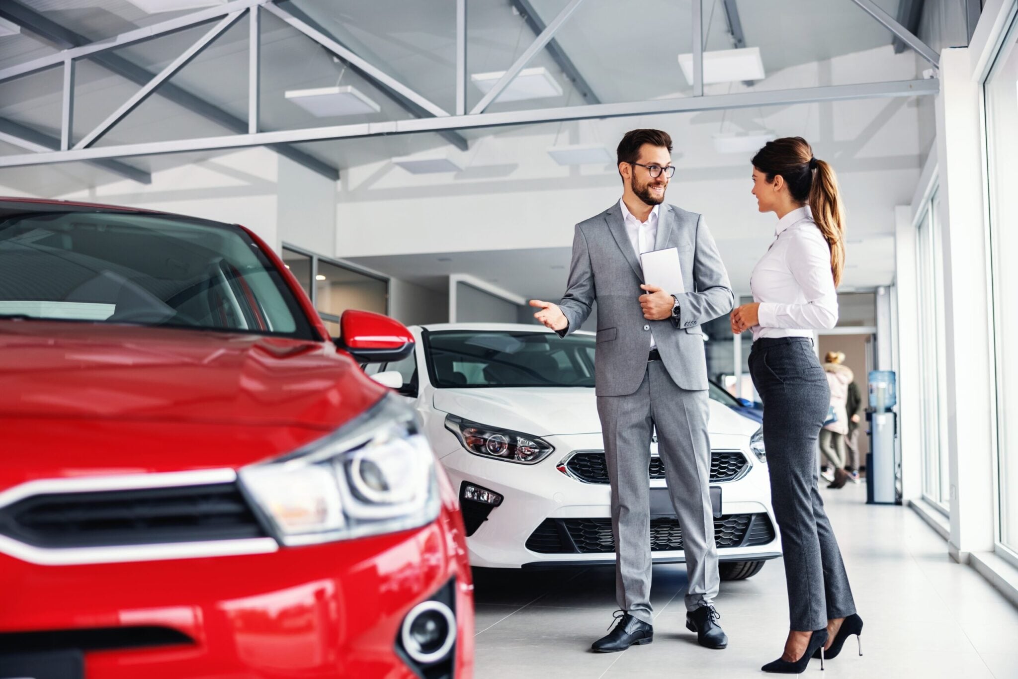 Smiling,Car,Seller,Standing,In,Car,Salon,With,Customer,And