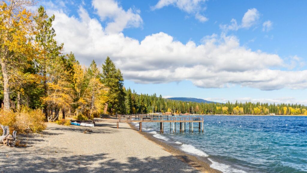 Wooden piers on a deserted pebble beach bordered with colourful woodland on a lake on a sunny and windy autumn day. Autumn colours. Lake Tahoe, CA, USA
