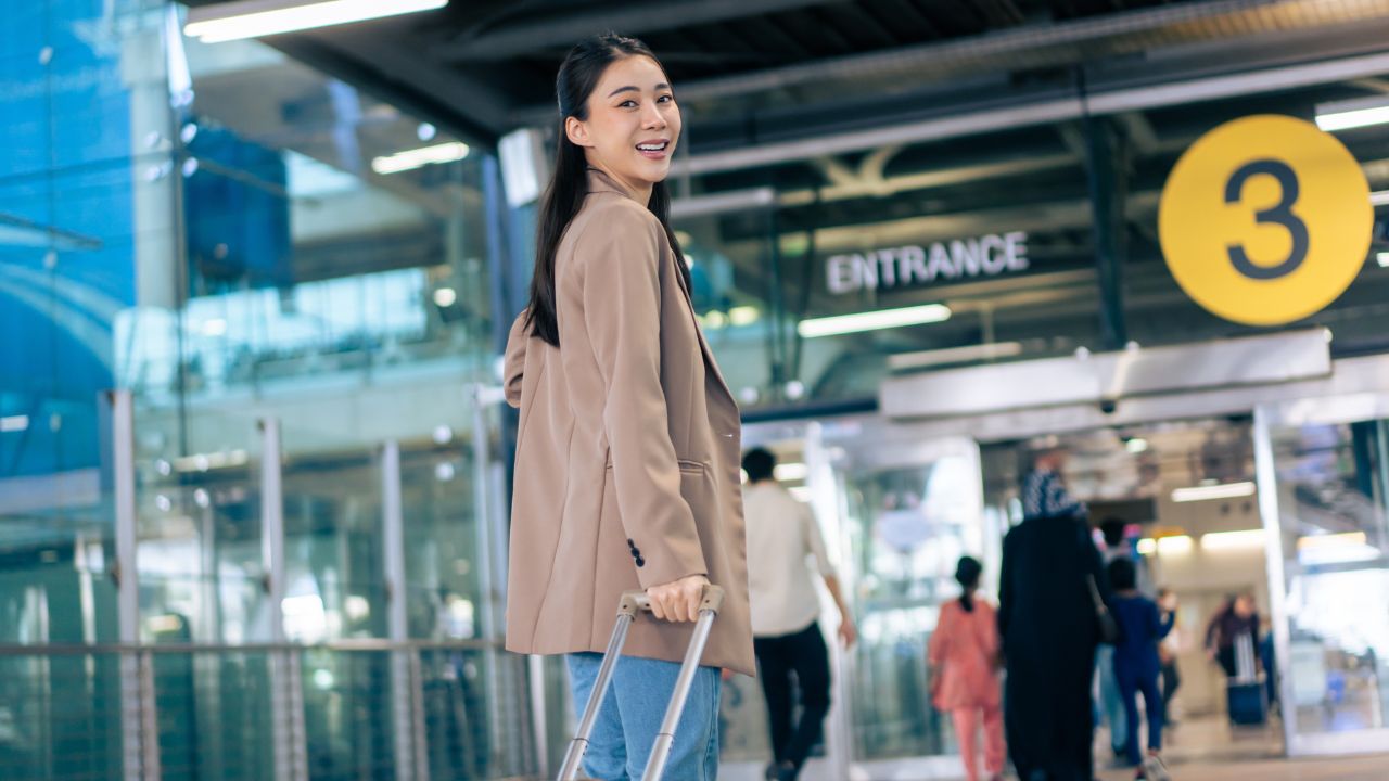 Portrait of Asian young girl walk in airport terminal to boarding gate. Attractive beautiful female tourist passenger feel happy and excited to go travel abroad by airplane for holiday vacation trip.
