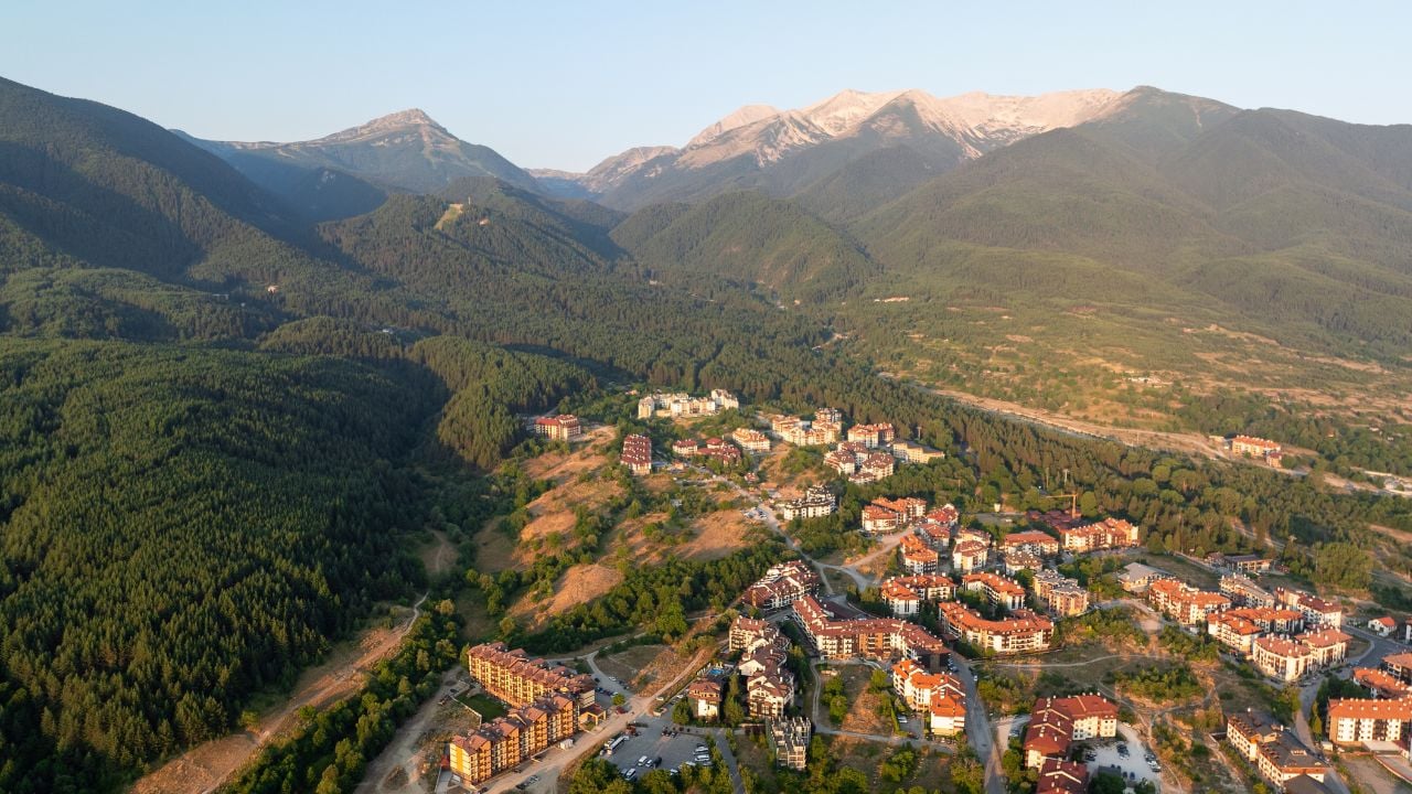 Bansko, Bulgaria, seen from above at dawn. Soft morning light highlights rooftops, mountains, and distant valley, capturing perfect harmony of historic town and surrounding nature. Travel