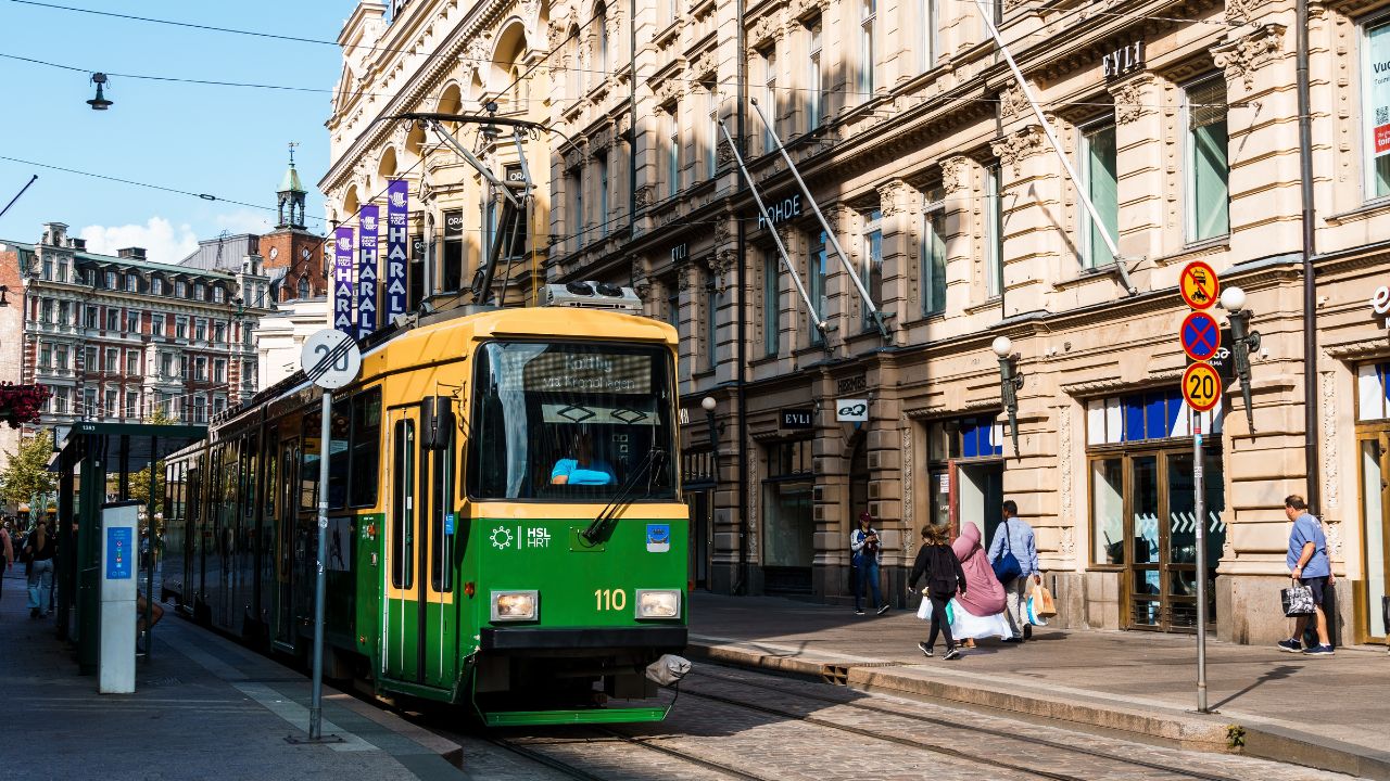 Helsinki, Finland - August 19, 2024: A green and yellow tram travels along a street in Helsinki, Finland with pedestrians walking by and historic buildings in the background.