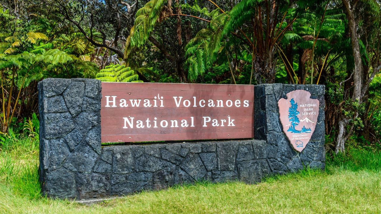 The Sign for Hawaii Volcanoes National Park in front of a vibrant green meadow.