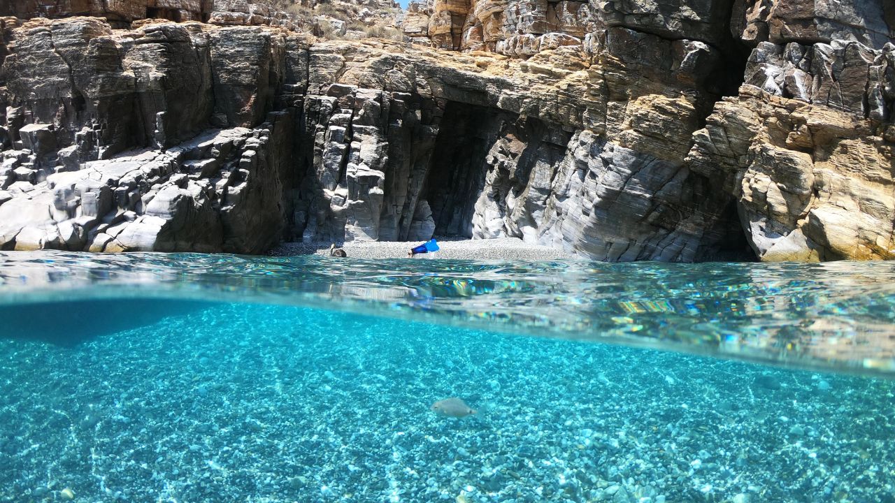 Above and below underwater photo of crystal clear sea paradise rocky seascape full of caves beach of Mouros, Amorgos island, Cyclades, Greece
