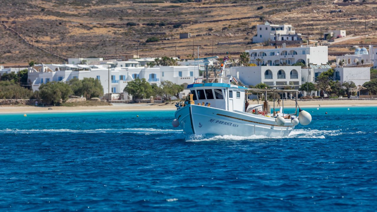 Koufonisi island, Cyclades, Greece. May 23, 2021. Sailing fishing boat in blue Aegean sea. Sandy beach sunny day mountains traditional village background. Summer destination for vacation.