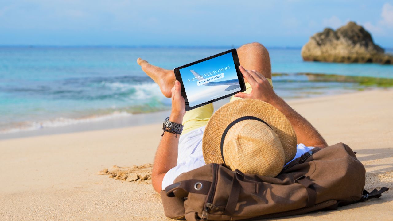 Man buying airline tickets online on tablet while relaxing on beach