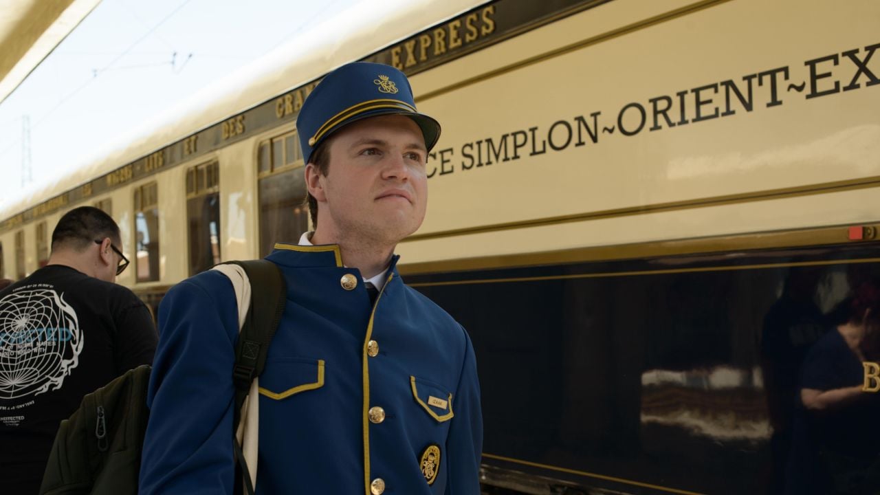 06-03-2025 - Ruse, Bulgaria: Venice Simplon Orient Express steward in blue gold uniform beside cream navy carriage, reflecting Art Deco luxury and premium European rail travel.