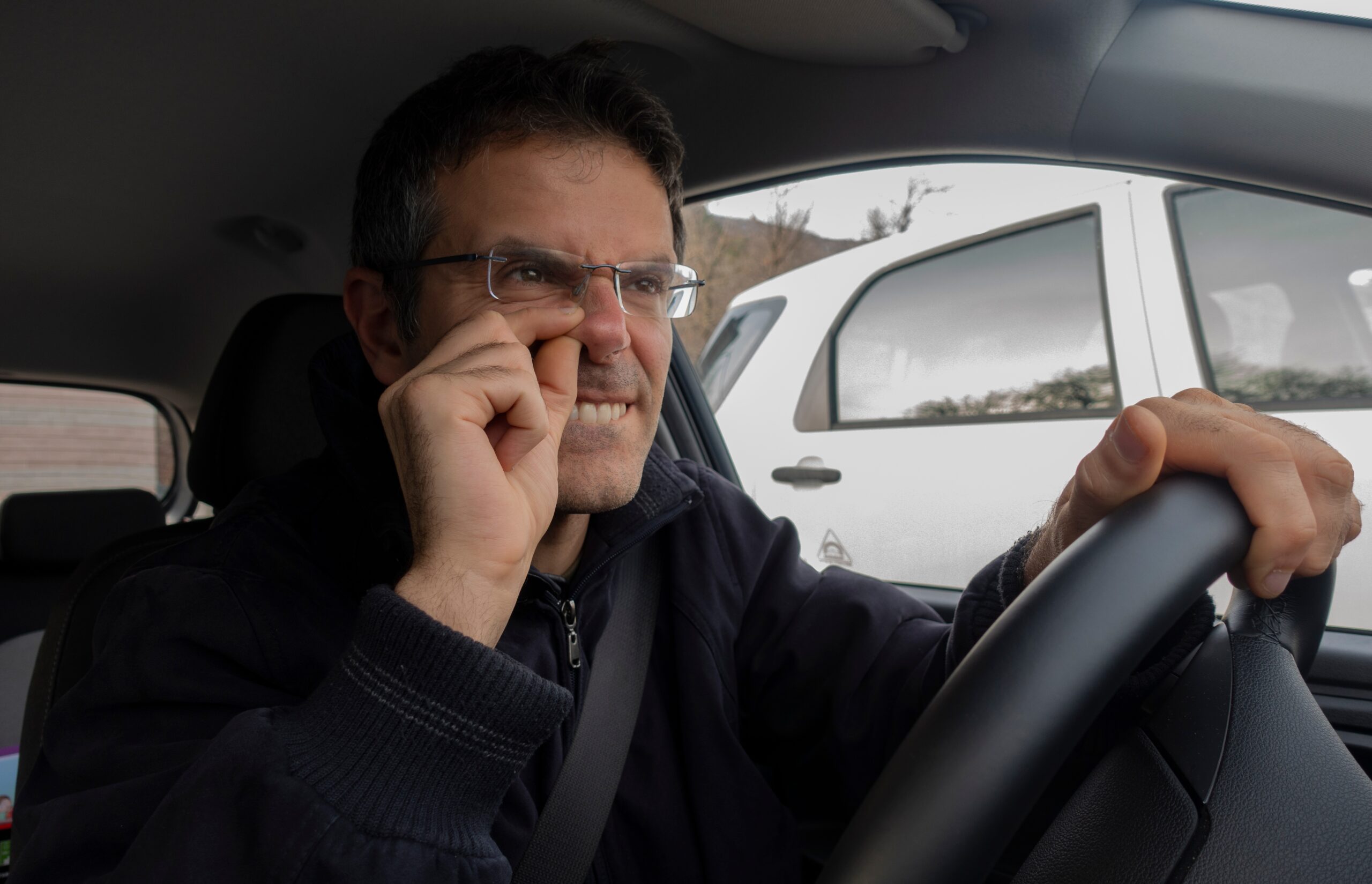 man picking nose in car