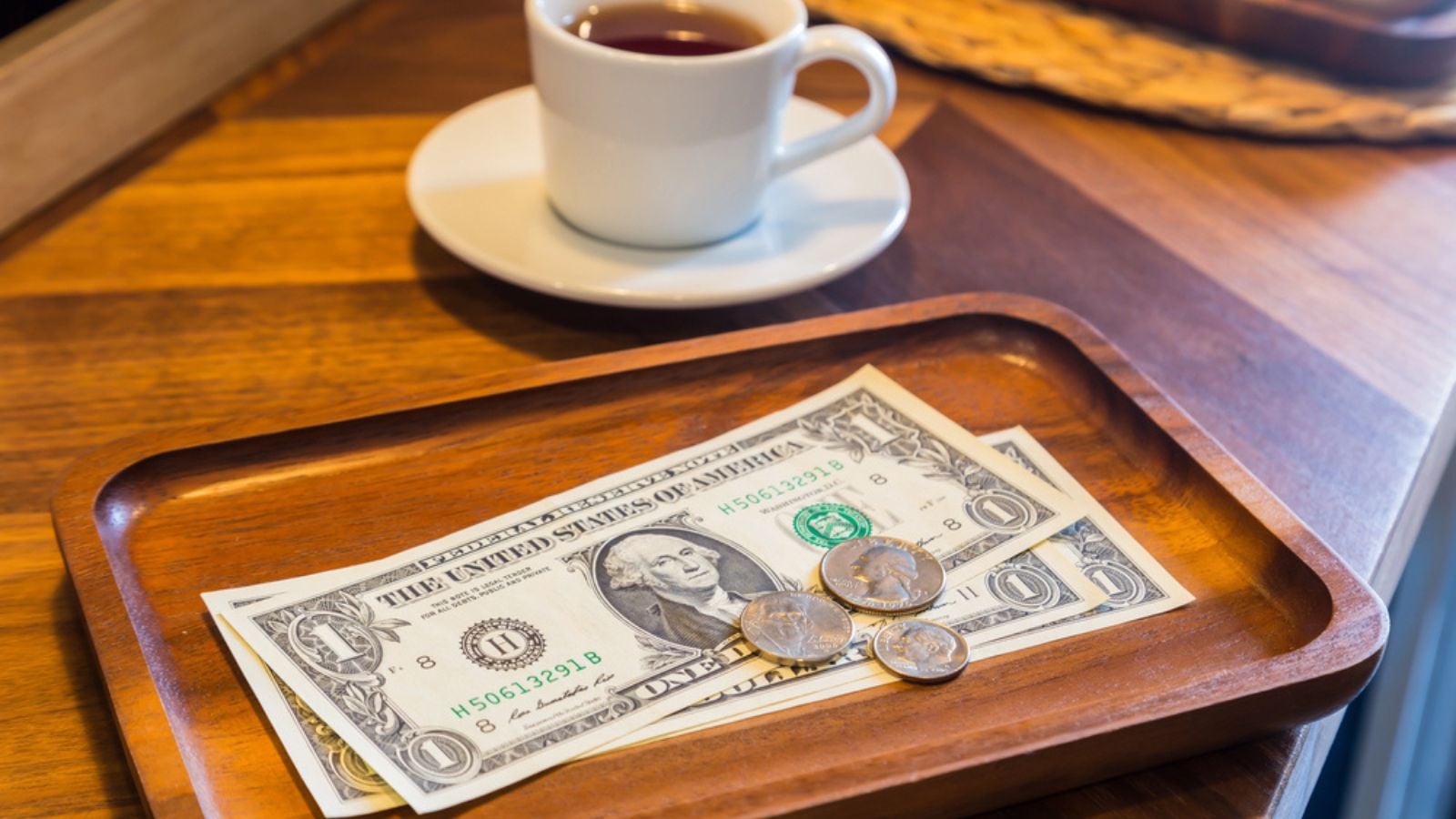 Dollar-banknotes-and-US-coins-on-wooden-tray-on-coffee-shop-table-with-a-white-cup-of-tea-on-background.-Concepts-for-customer-service-checking-money-t