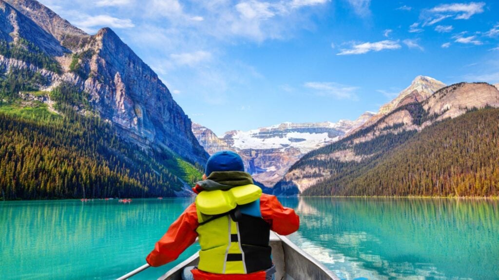 Teen boy canoeing on Lake Louise in Banff National Park of the Canadian Rockies with its glacier-fed turquoise lakes and Mount Victoria Glacier in the background