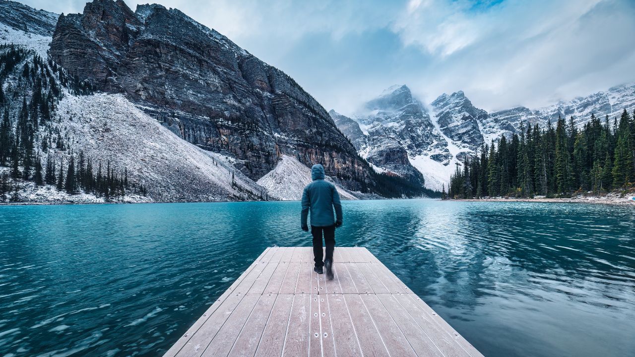 Lonely traveler man walking on pier surrounded by Rocky mountains on Moraine Lake at Banff national park, Alberta, Canada