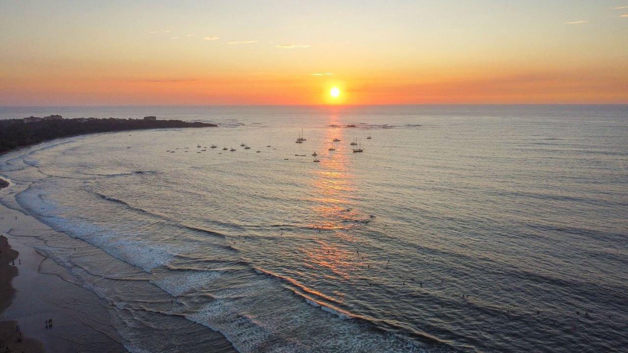 A serene sunset over Tamarindo Beach, Costa Rica, with gentle waves and boats on the horizon.