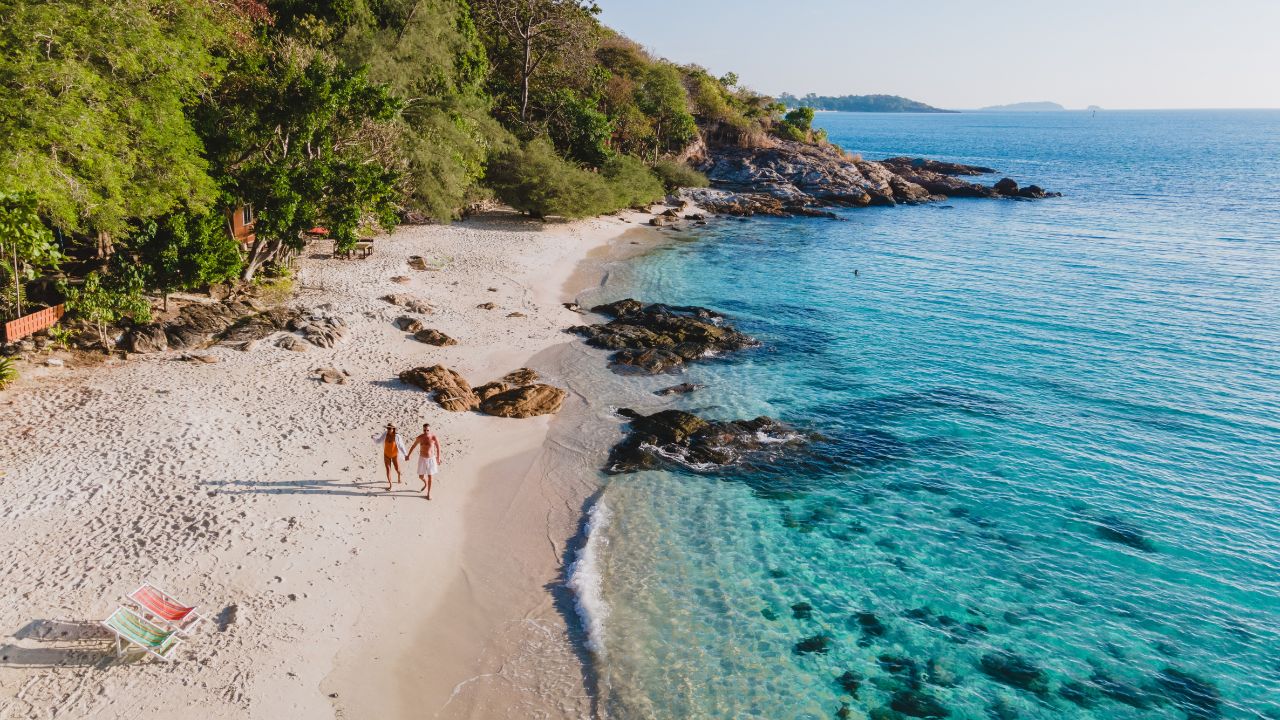 Koh Samet Island Thailand, aerial drone view from above at a couple of men and woman walking on the beach of Samed Island in Thailand with a turqouse colored ocean and a white tropical beach
