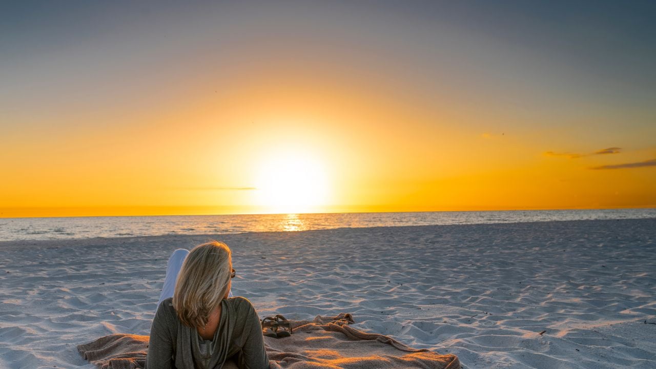 Woman laying on blanket at the beach looking at the sunset