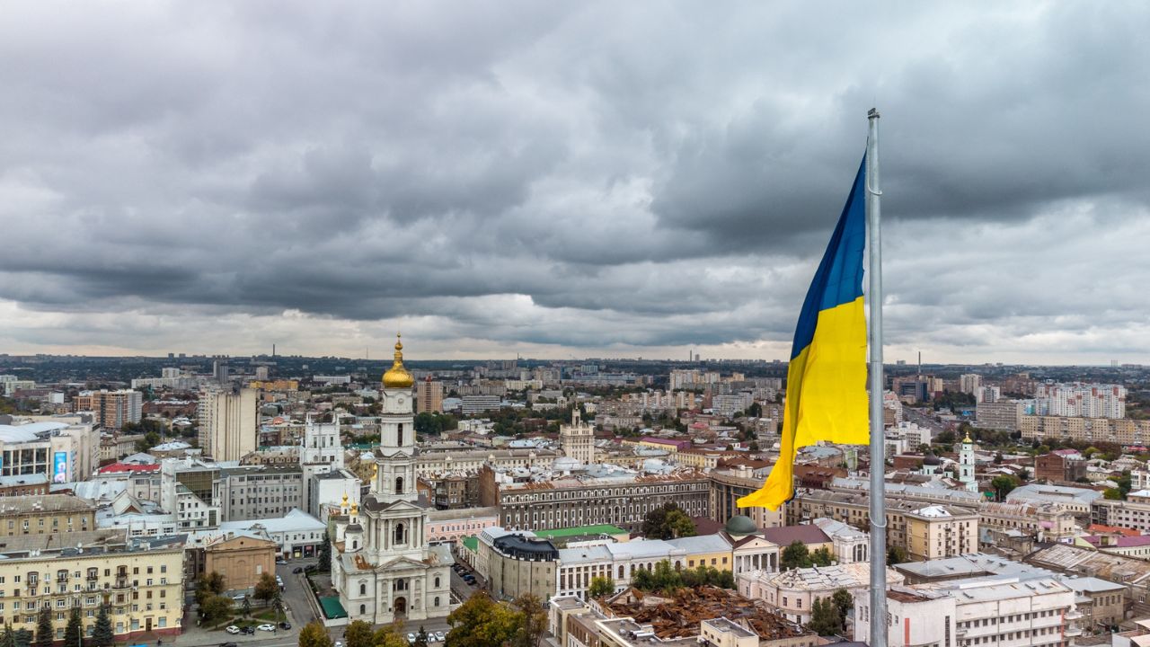 Flag of Ukraine close-up with autumnal epic gray cloudscape, city aerial view near river Lopan embankment, Dormition Cathedral in Kharkiv, Ukraine