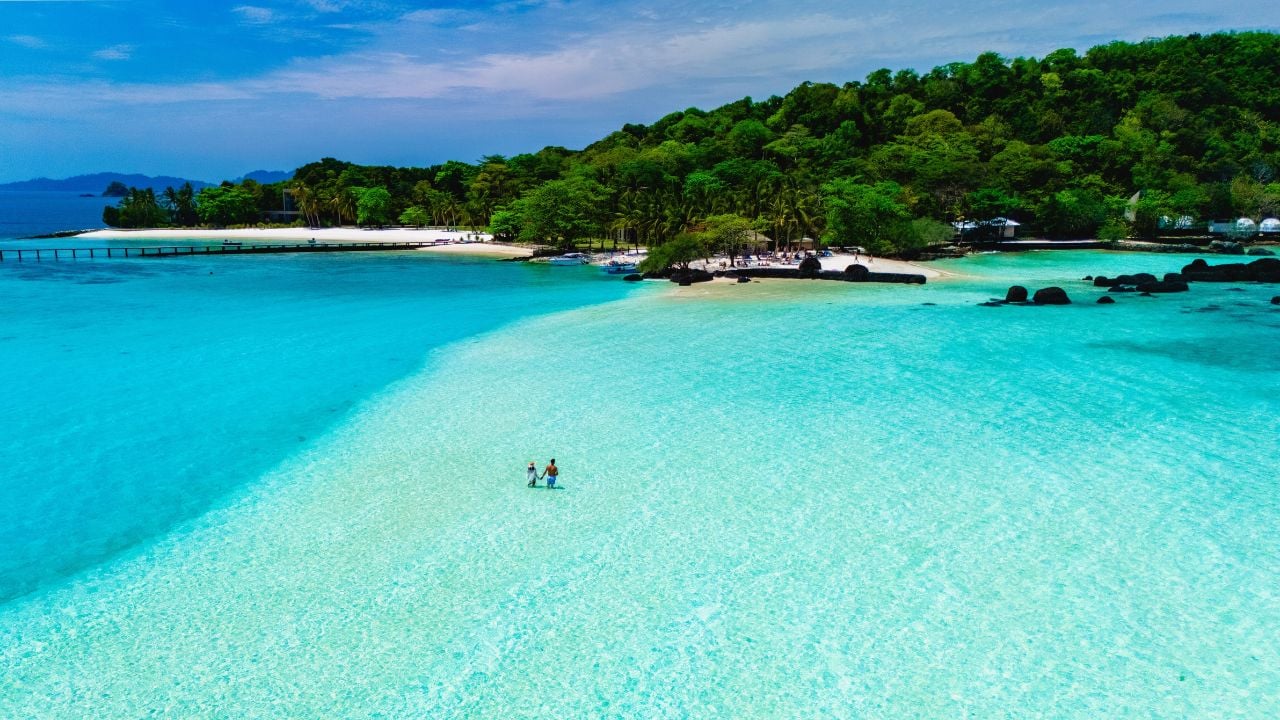 Two people standing on pristine white sand, surrounded by crystal-clear turquoise waters. Koh Kham Island near Koh Mak Thailand