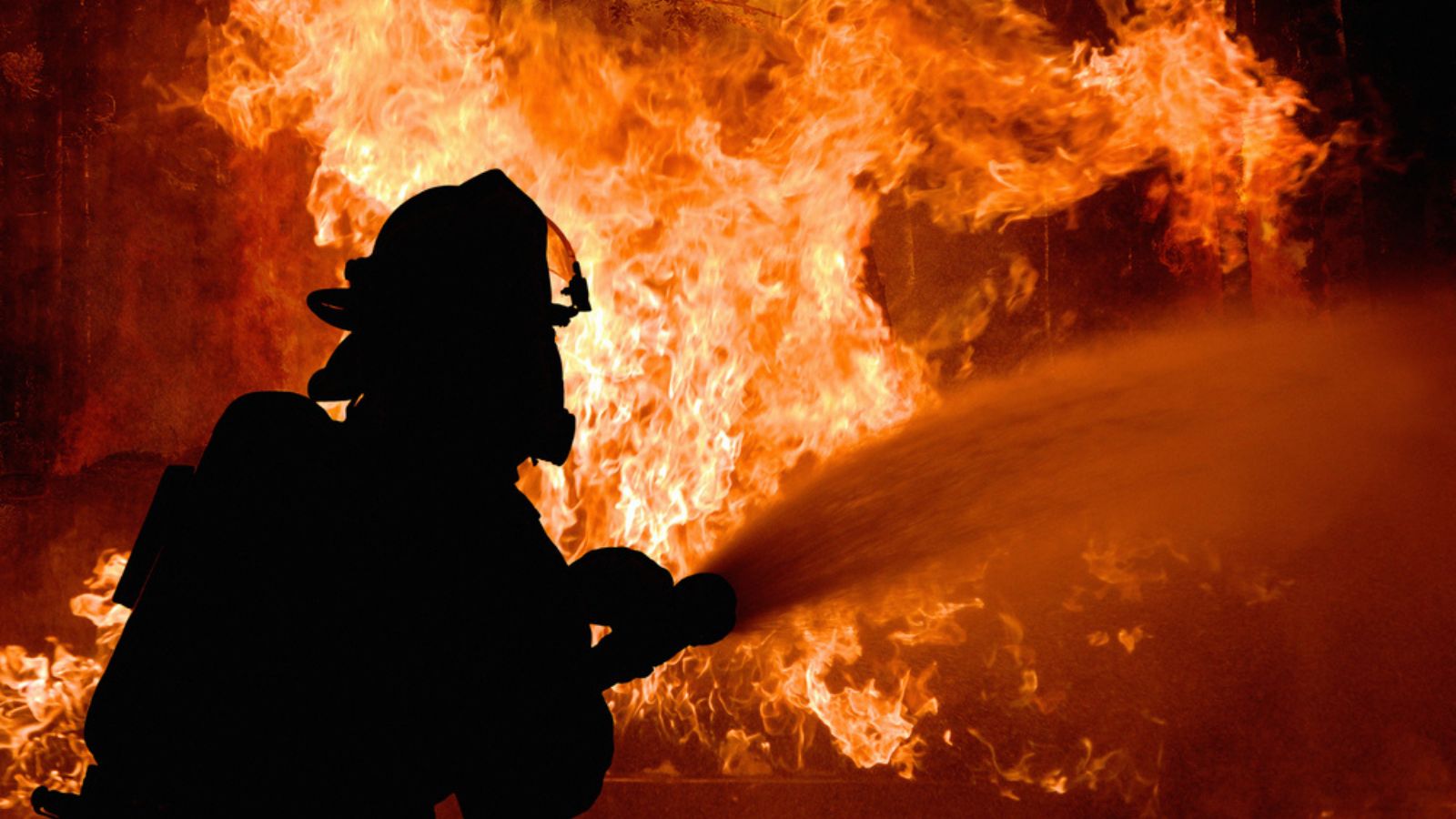 Silhouette of Firemen fighting a raging fire with flames