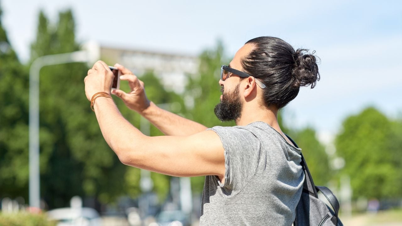 leisure, technology and people concept - hipster man taking picture or video by smartphone on street