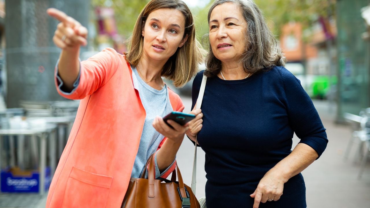 Friendly girl helping elderly woman to find necessary address in city, pointing direction with hand.