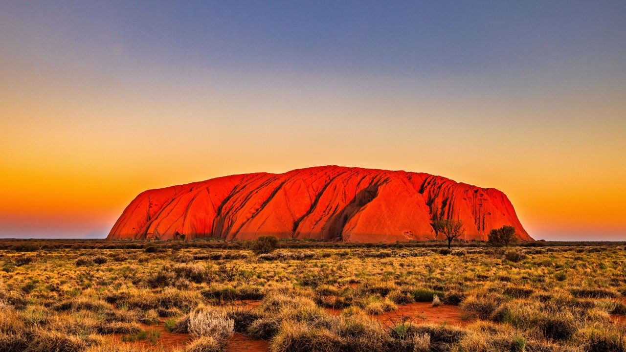 Uluru at sunset with vibrant orange hues and a clear sky in the Australian outback.