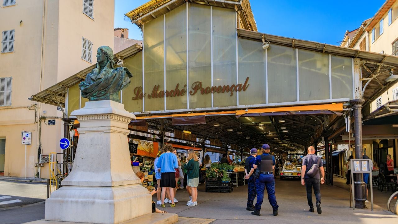 Antibes, France - May 24, 2023: Covered provencal market hall on Cours Massena in the old town Vieil Antibes, shoppers going in and police outside