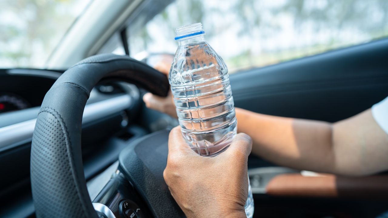 Asian woman driver holding bottle for drink water while driving a car. Plastic hot water bottle cause fire.