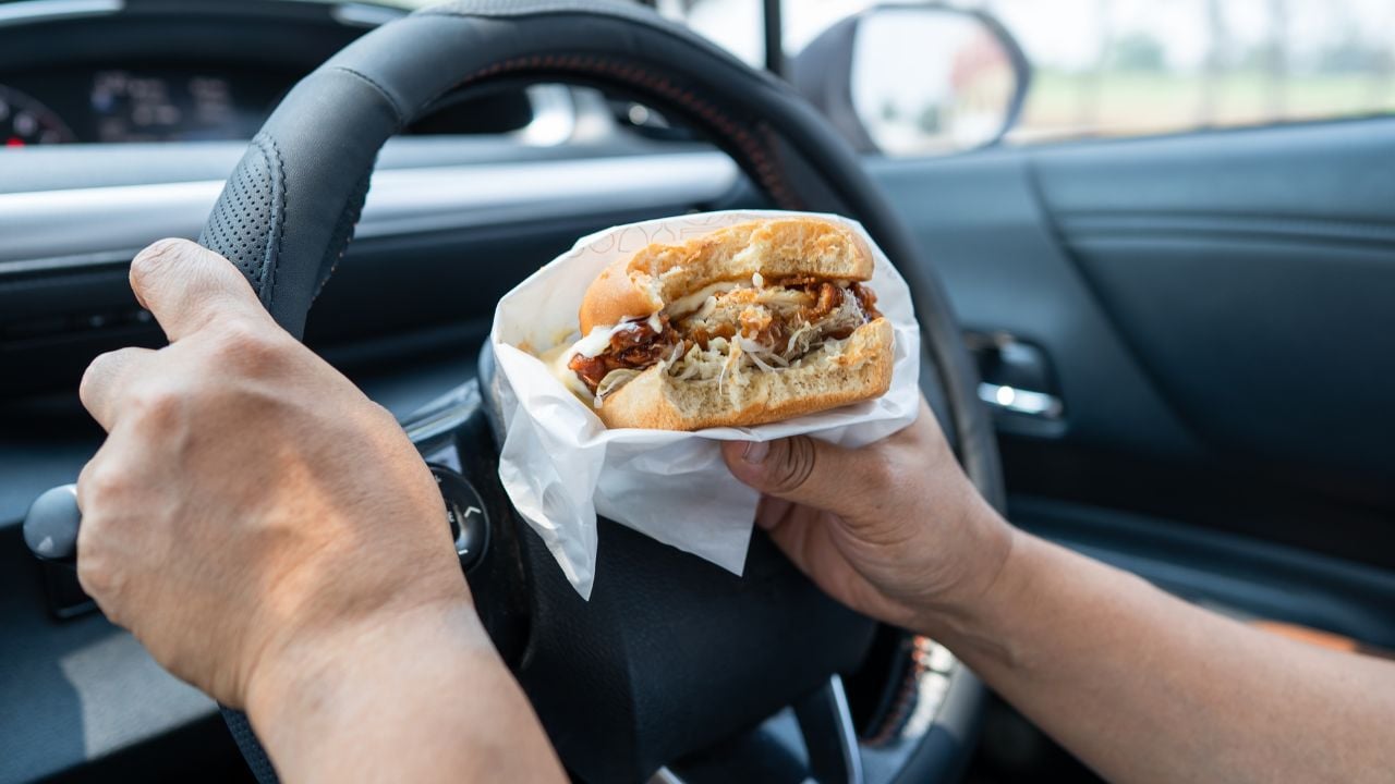 Asian lady holding hamburger and French fries to eat in car, dangerous and risk an accident.