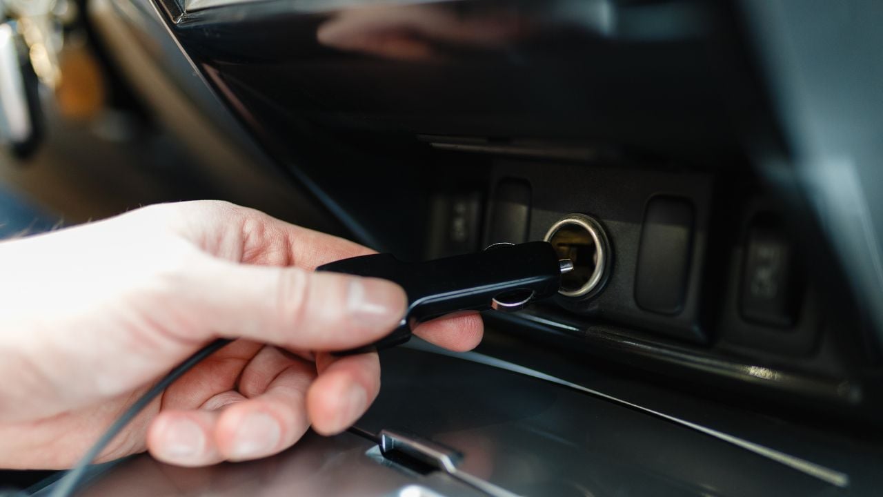 A man connects the device to the cigarette lighter of the car. The man's hand is plugging the car camera or phone adapter into the cigarette lighter into the car.