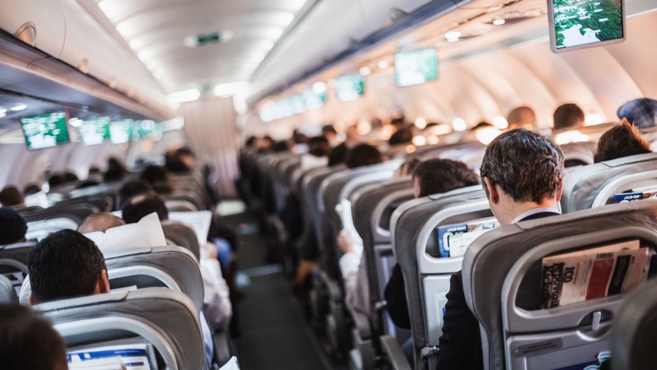 Interior of airplane with passengers on seats and stewardess in uniform walking the aisle, serving people. Commercial economy flight service concept