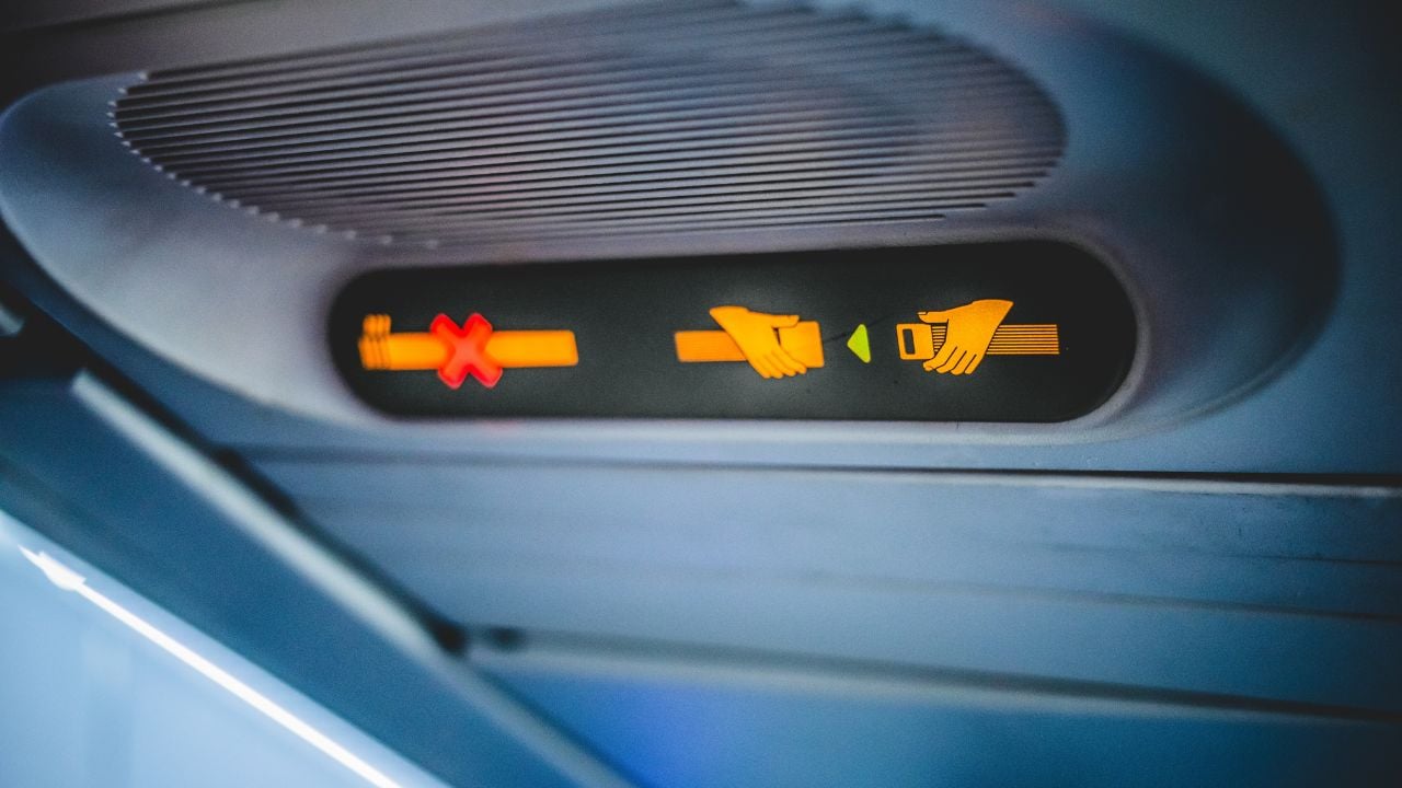 Close-up of an illuminated fasten seatbelt sign inside an airplane cabin, instructing passengers to buckle up for safety during the flight.