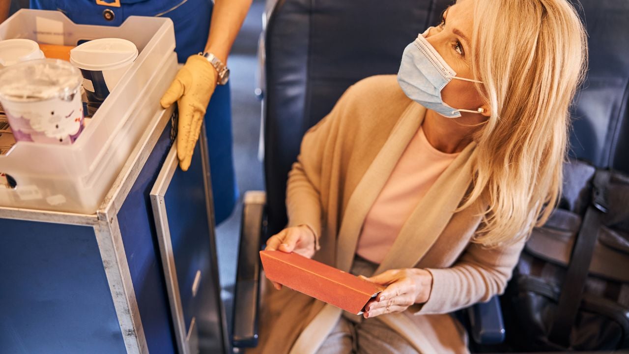 Cropped photo of a Caucasian female throwing away a biscuit package to a rubbish trolley of a flight attendant