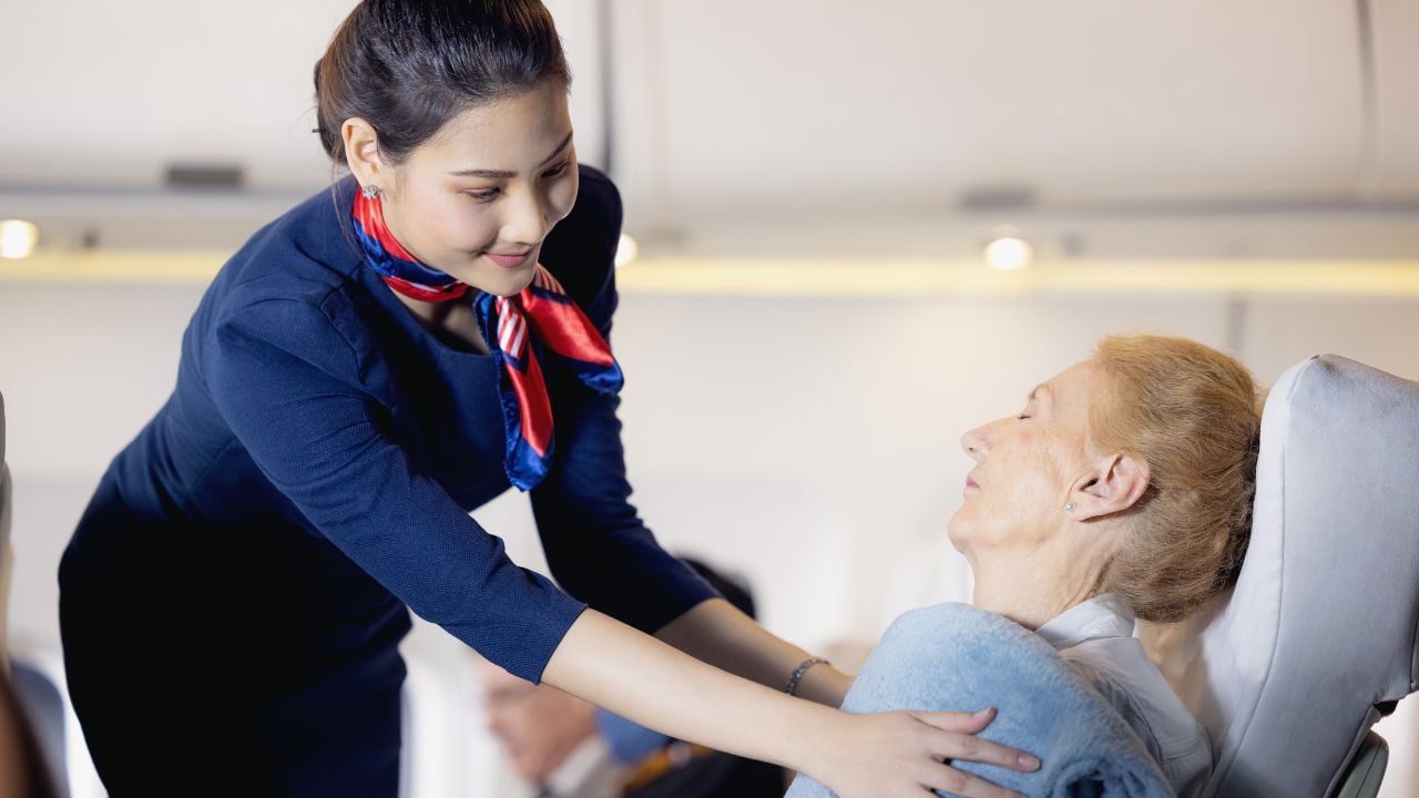 A female flight attendant clothed an elderly passenger sleeping in the passenger seat. Stewardess taking care of the passenger. Cabin crew gives service to a passenger in an airplane.