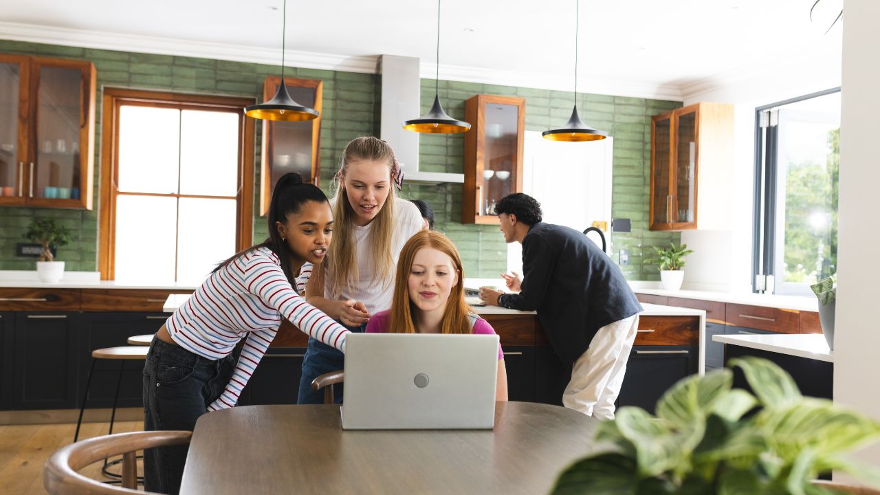 In modern kitchen, teen friends collaborating on laptop, focusing on teamwork. Technology, friendship, collaboration, digital, youth, innovation