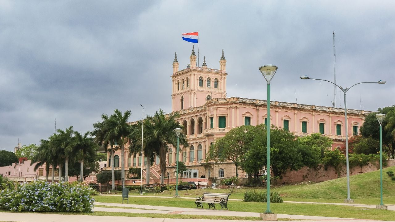 Historic government building with Paraguayan flag in Asuncion's green park on a cloudy day
