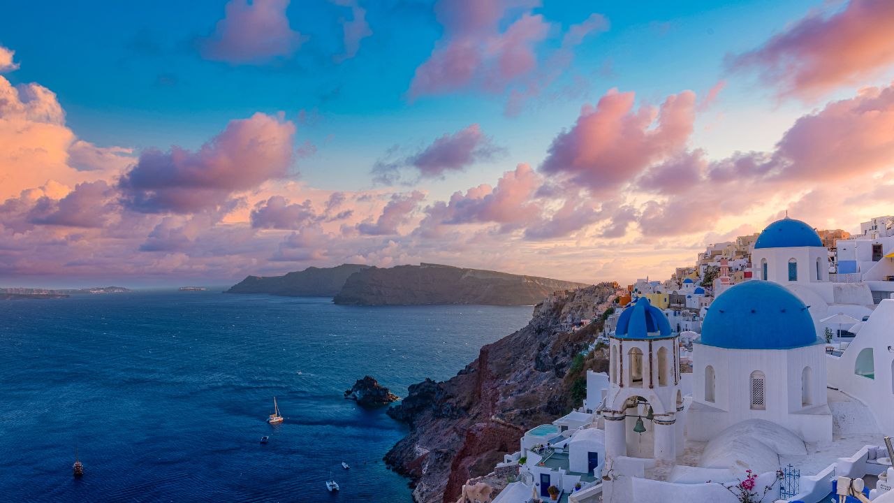 Beautiful panorama view of Santorini island in Greece at sunrise with dramatic sky. Stunning Oia cityscape, sunset colors sky with blue domes with white architecture. Amazing travel vacation landscape