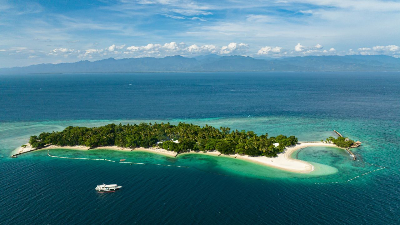 White sand around the island. Boat over the blue sea, blue sky and clouds. Samal Island. Davao, Philippines.