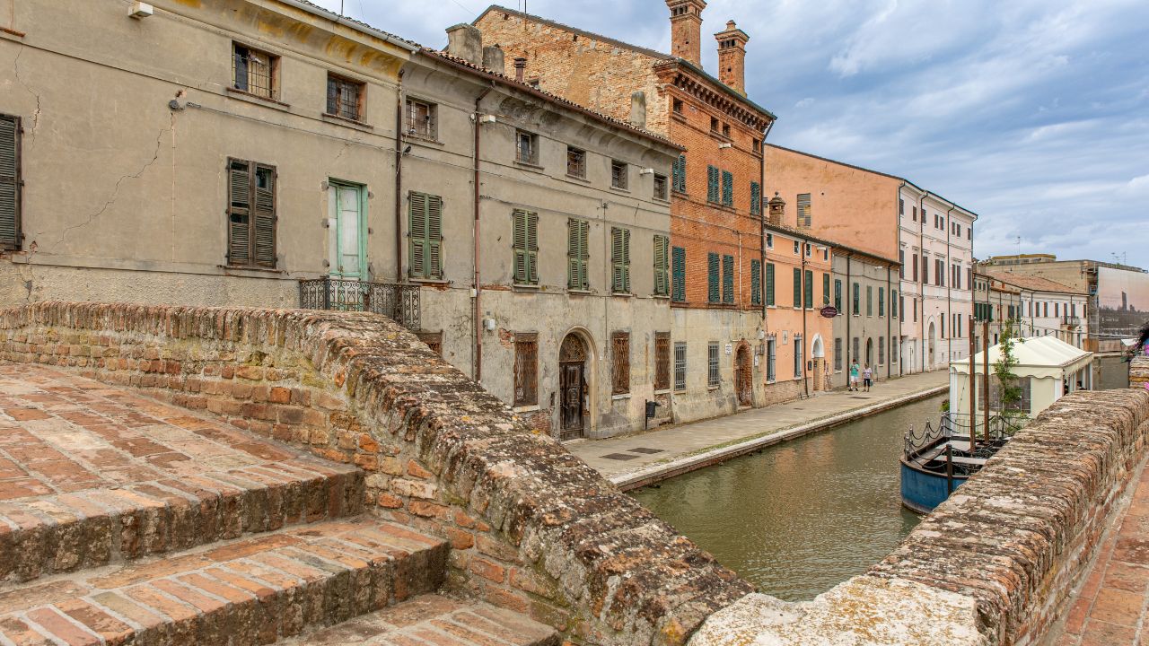 Comacchio, Italy, 08 24 2025, historic canal view with old colorful houses, brick bridge and reflections in the water, capturing the charm of the little Venice of Emilia-Romagna.