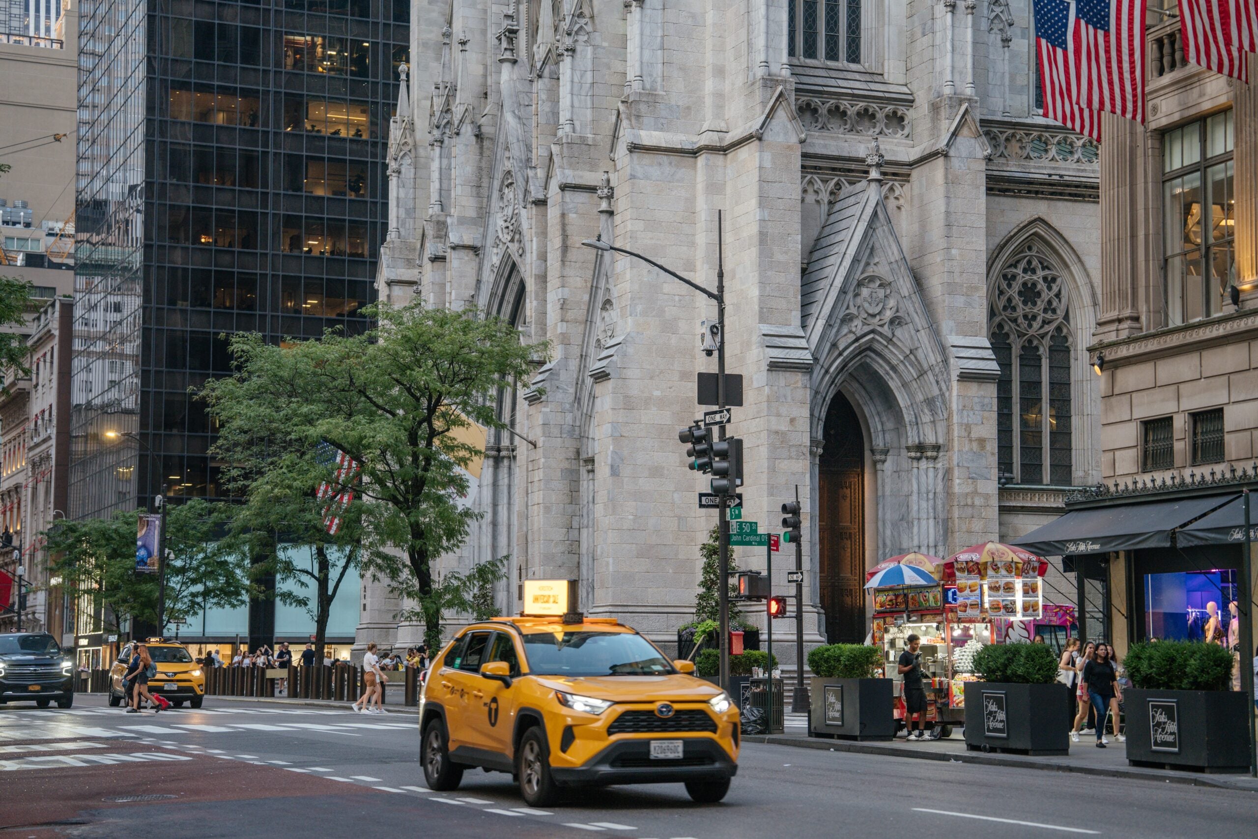New York City, New York, USA - 07.29.2024: A yellow NYC taxi drives past the grand entrance of St. Patrick's Cathedral on Fifth Avenue. The Gothic-style cathedral stands proudly beside modern